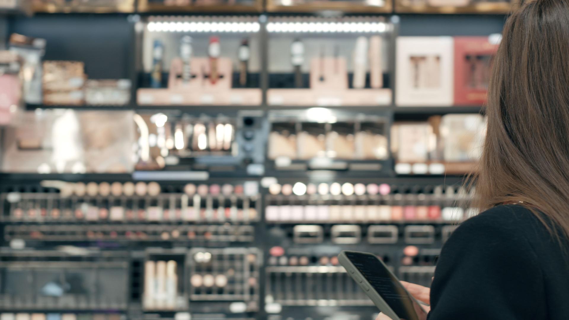 Woman using a smartphone and choosing cosmetics in a store